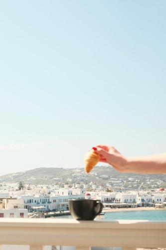 a persons hand holding a piece of food on a balcony at Yalos Hotel Sunset view Mykonos town private rooms in Mýkonos City