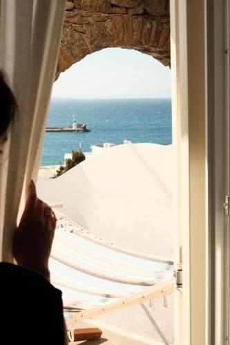 a person looking out a window at the ocean at Yalos Hotel Sunset view Mykonos town private rooms in Mýkonos City