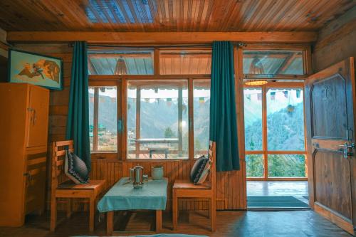 una stanza con un tavolo, sedie e finestre di Negi Farmhouse Shangarh a Sainj