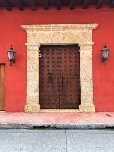 a red wall with a wooden door and two lights at Tranquila y cerca de la magia in Cartagena de Indias