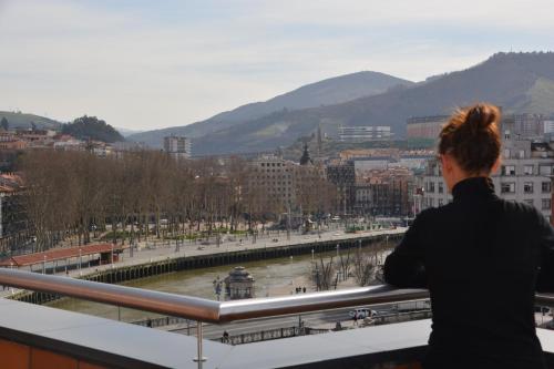 a woman standing on a balcony looking at a city at Hotel Bilbao Plaza in Bilbao