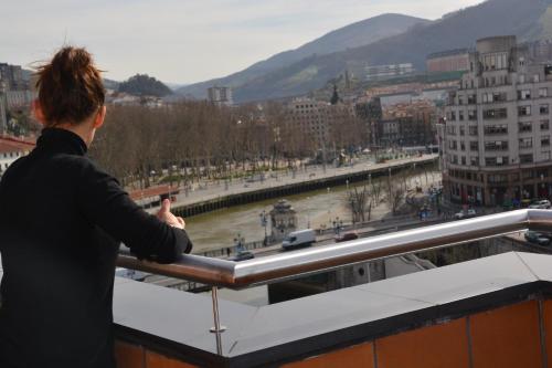 a woman standing on a roof taking a picture of a river at Hotel Bilbao Plaza in Bilbao