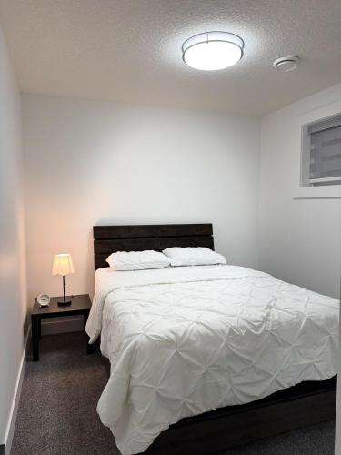 a bedroom with a large white bed with a lamp at Charming Basement Suite in Edmonton