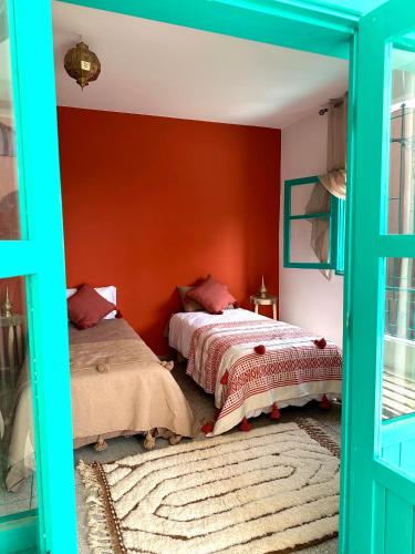 two beds in a room with a red wall at Dar Al-Andalus in Tamraght Ouzdar