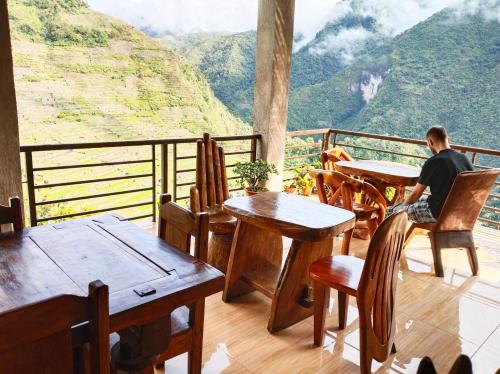 un hombre sentado en mesas en un balcón con vistas en Batad Pension and Restaurant Native House, en Banaue