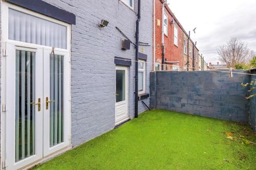 a backyard with a grass yard next to a brick building at 17 Anfield House sleeps 12 7min walk to stadium in Liverpool