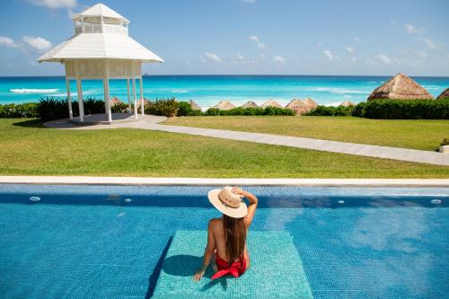 a woman in a hat sitting next to a swimming pool at Paradisus Cancun All Inclusive in Cancún