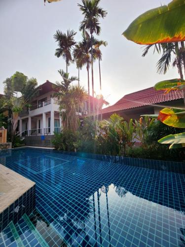 a swimming pool in front of a house with palm trees at Cocoville Phuket - SHA Plus in Chalong