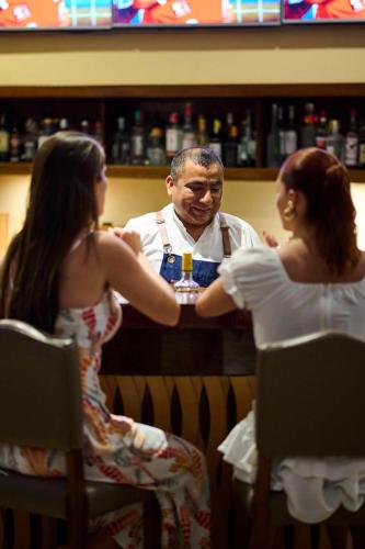 a man in a bar holding a drink in front of two women at Casa Andina Standard Chincha in Chincha Alta