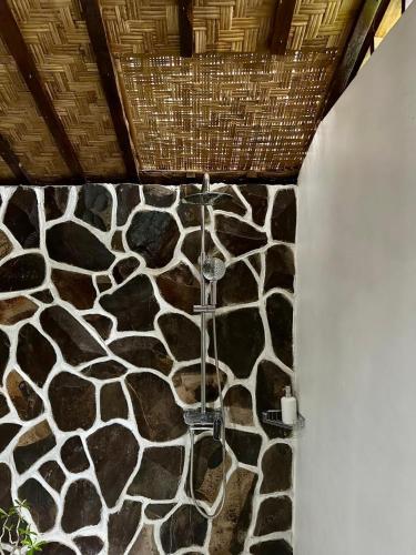 a bathroom with a shower with a stone wall at Beehive Cottages in Amed