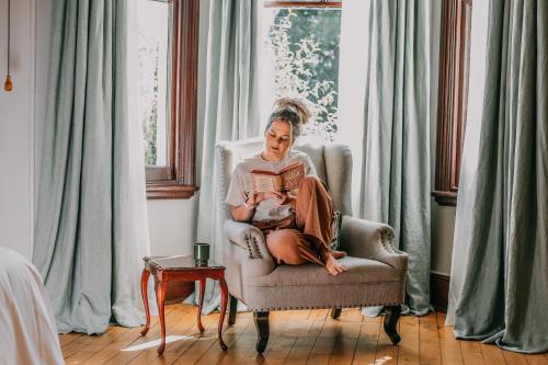 a woman sitting in a chair reading a book with a baby at Littlebourne Guest House in Bathurst