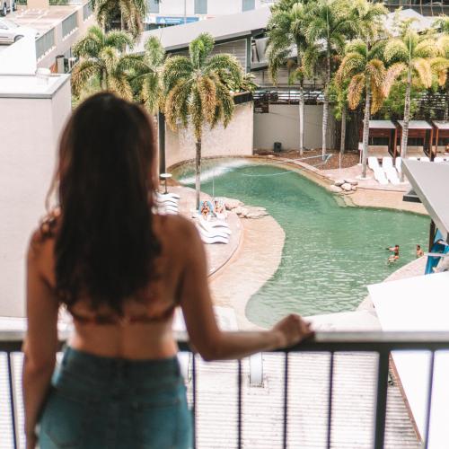 a woman standing on a balcony looking at a swimming pool at Gilligan's Hotel & Resort Cairns in Cairns