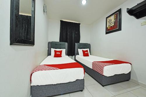 two beds in a room with white walls and red pillows at Hotel O Gemilang in Kuala Terengganu