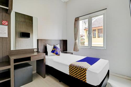 a bedroom with a bed and a desk and a window at Hotel O Cihampelas Near Ciwalk Formerly D'River Guest House in Bandung