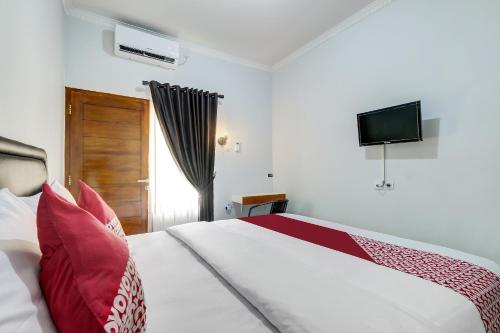 a bedroom with a bed with red pillows and a television at Capital O 90983 Harmony Easy Stay in Yogyakarta