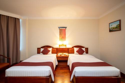 two beds in a hotel room with a lamp between them at Khemara Angkor Hotel & Spa in Siem Reap