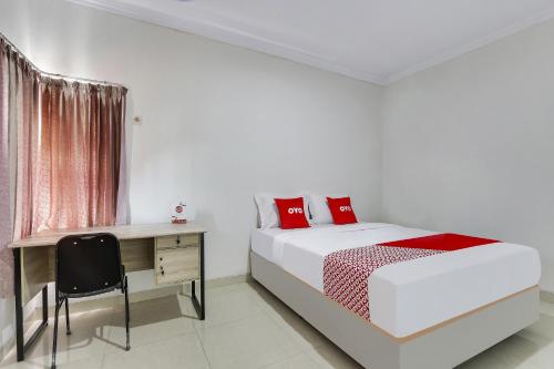 a white bedroom with a bed and a desk at Hotel O Nathania Exclusive in Sleman