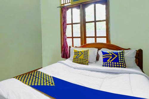 a bed with blue and yellow pillows and a window at OYO Homes 91154 Desa Wisata Wayang Manyaran Wonogiri in Wonogiri