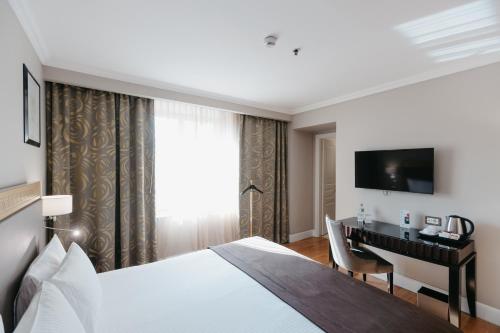 a hotel room with a bed and a desk and a television at Grand Hotel Yerevan - Small Luxury Hotels of the World in Yerevan