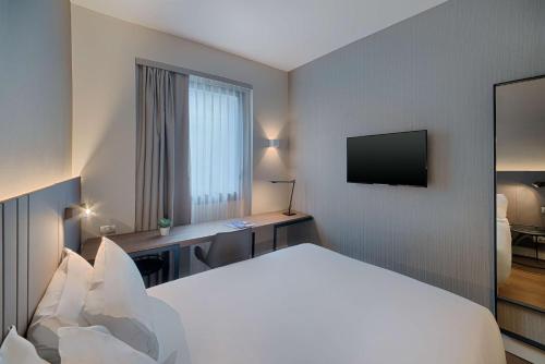 a hotel room with a bed and a desk with a television at NH Palermo in Palermo