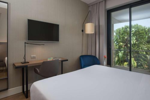 a hotel room with a bed and a desk and a window at NH Palermo in Palermo