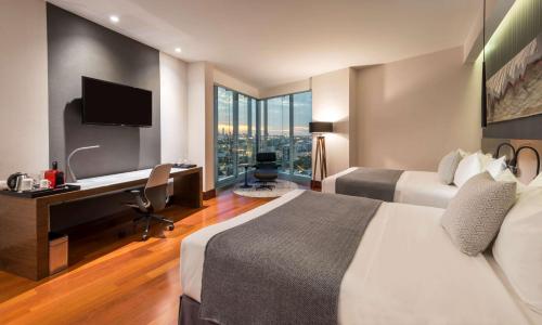 a hotel room with two beds and a desk with a computer at NH Collection Guadalajara Providencia in Guadalajara