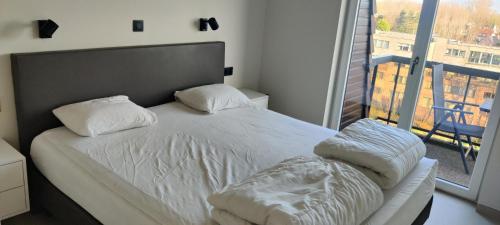 a bed with white sheets and pillows in a room with a window at Recent vernieuwd appartement met zeezicht en een gratis parkeerplaats in Koksijde