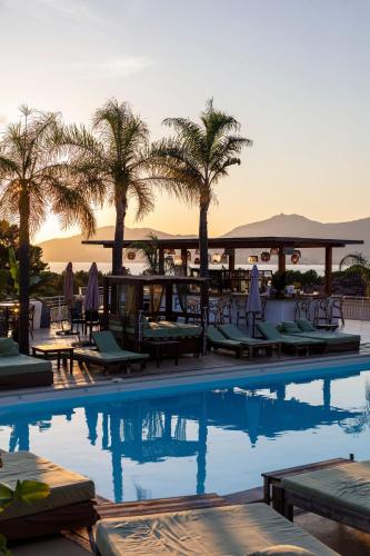 a swimming pool with chairs and palm trees and the sunset at Bella Vista Hôtel, Suites & Maisons in Porticcio