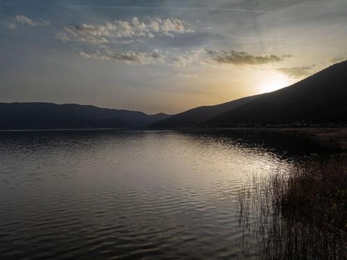 a body of water with the sun setting behind mountains at Prespes Lake View Family Apartment in Florina