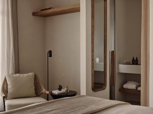 a bedroom with a bed and a chair and a mirror at Stamna Sifnos a member of Design Hotels in Sifnos