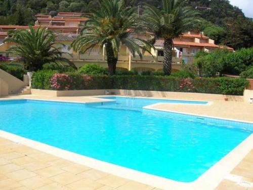 une grande piscine bleue avec des palmiers et un bâtiment dans l'établissement Appartement T2, 4 personnes terrasse vue mer résidence avec piscine à Pramousquier - LE LAVANDOU, au Lavandou