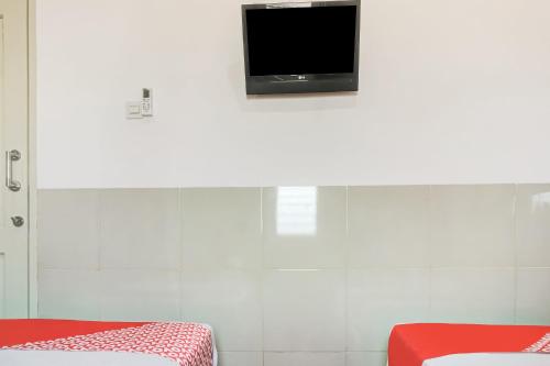 a room with two beds and a tv on the wall at OYO 91316 Hh Guest House Makassar in Makassar