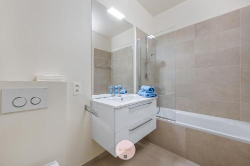a white bathroom with a sink and a tub at Osean by BLOSS luxe appartement met frontaal zeezicht, binnenzwembad en parking in Middelkerke