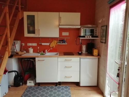 - une petite cuisine avec des placards blancs et des murs rouges dans l'établissement L atelier de PELLICA, à Lit-et-Mixe