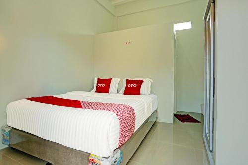 a white bedroom with a large bed with red pillows at OYO 91434 Cek@n Guest House in Banda Aceh