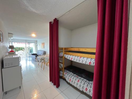 Cette chambre comprend 2 lits superposés dotés de rideaux rouges. dans l'établissement Appartement 2P cabine, face plage, clim, parking privatif - FR-1-338-609, à Sète