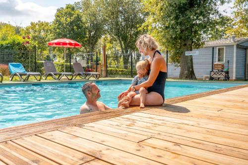 una mujer, un hombre y un niño sentados en una piscina en Camping des Salines, en Salies-de-Béarn