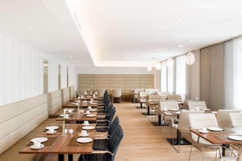 a restaurant with wooden tables and white chairs at NH Collection Wien Zentrum in Vienna