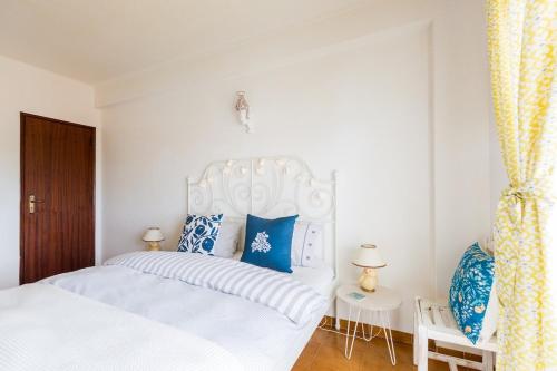 a bedroom with a white bed with blue pillows at Bright Apartment 10min from 2 stunning Beaches in Olhos de Água