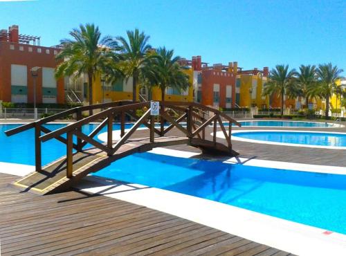 a wooden bridge over a swimming pool with palm trees at Apartamento Vera-playa in Los Amarguillos