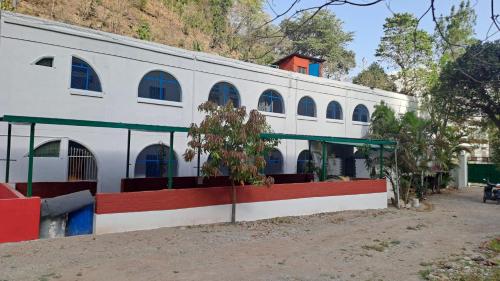 a white building with blue windows and plants in front at Swami Samarpan Ashram in Rishīkesh