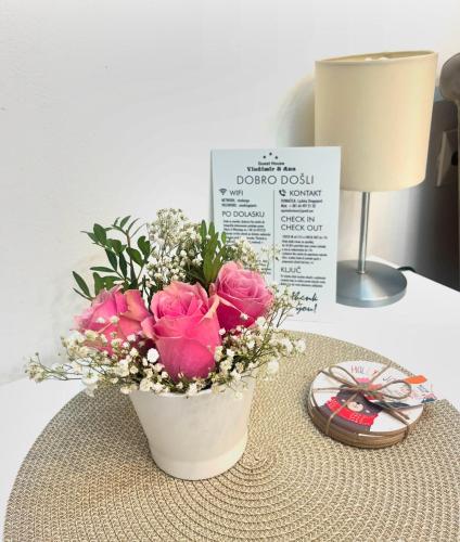a white vase with pink flowers on a table at Guesthouse Vladimir & Ana in Pančevo