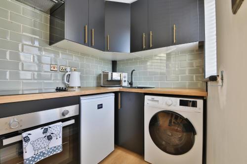 a kitchen with black cabinets and a washer and dryer at Luxury Cosy Central Detached Cardiff Bungalow with Free Parking in Cardiff
