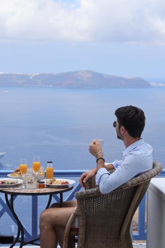 a man sitting at a table with food and drinks at Golden Grey Goose in Fira