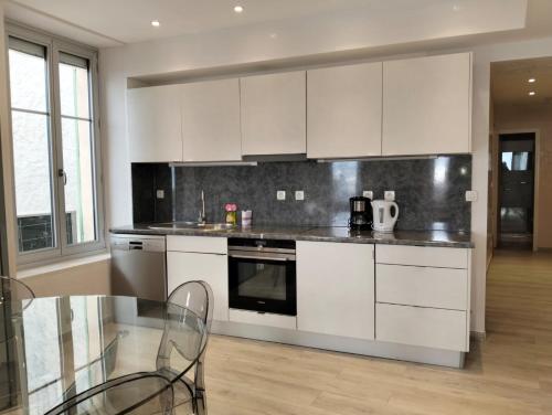 une cuisine avec des armoires blanches et une table en verre dans l'établissement PLEIN SUD - Le FAURE, à Cannes