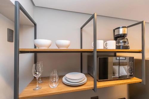 a shelf with a microwave and plates and glasses at Vibe Curitiba by Housi, próximo à Ligga Arena e Praça do Japão in Curitiba
