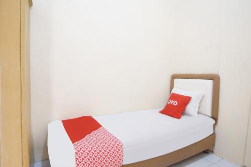 a small bedroom with a white bed with two red pillows at Hotel O Kost Ketapang Syariah in Medan