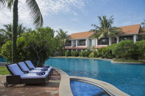 a swimming pool with two lounge chairs next to a resort at Radisson Blu Resort Temple Bay Mamallapuram in Mahabalipuram
