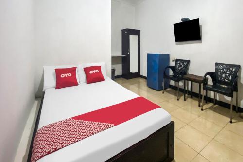 a bedroom with a bed and two chairs and a television at Hotel O We Bro Kost in Kupang