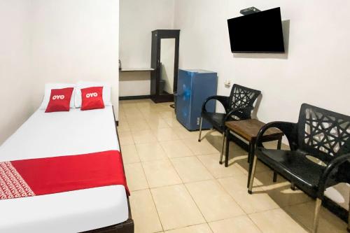 a room with a bed and two chairs and a television at Hotel O We Bro Kost in Kupang
